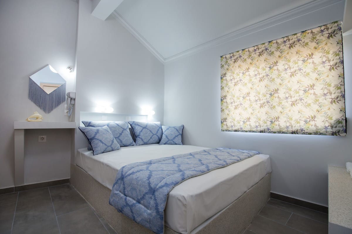 A bedroom with a bed, a bedside table, a mirror, and a window with floral curtains.