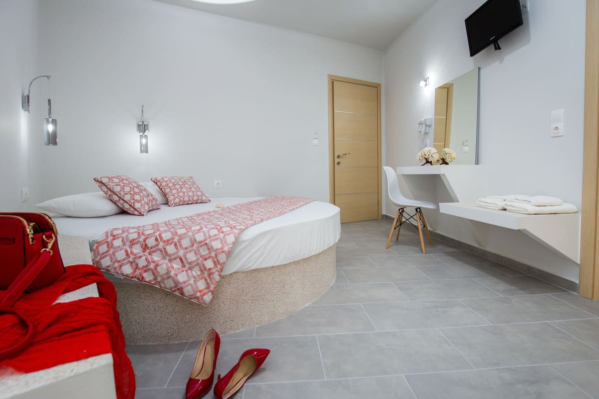 A modern bedroom with a curved bed, a vanity with a mirror, and a TV mounted on the wall.