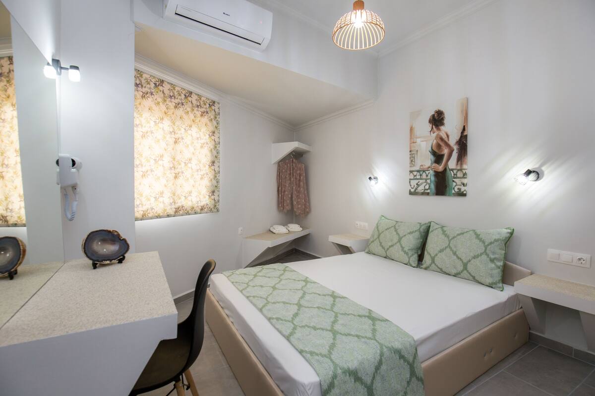 A bedroom with a bed, a desk, a chair, a vanity, and a window with curtains.