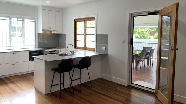 A modern kitchen with white cabinets, a central island with bar stools, a window, and a sliding glass door leading to an outdoor area. - House in Belmont fully renovated (Belmont)