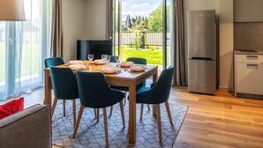 Ein moderner Essbereich mit einem Holztisch, gedeckt für vier Personen, umgeben von dunklen Stühlen. An der Wand ist ein Flachbildfernseher angebracht, und im Hintergrund ist ein Kühlschrank zu sehen.