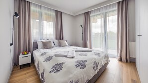 Ein modernes Schlafzimmer mit einem großen Bett, zwei Nachttischlampen, einem Nachttisch mit Obst und transparenten Vorhängen.