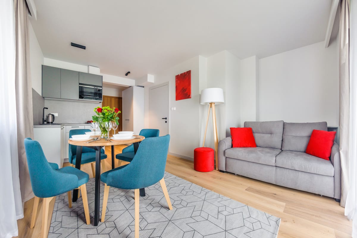 Uma sala de estar moderna com um sofá cinzento, cadeiras azuis e uma mesa de jantar com cadeiras.