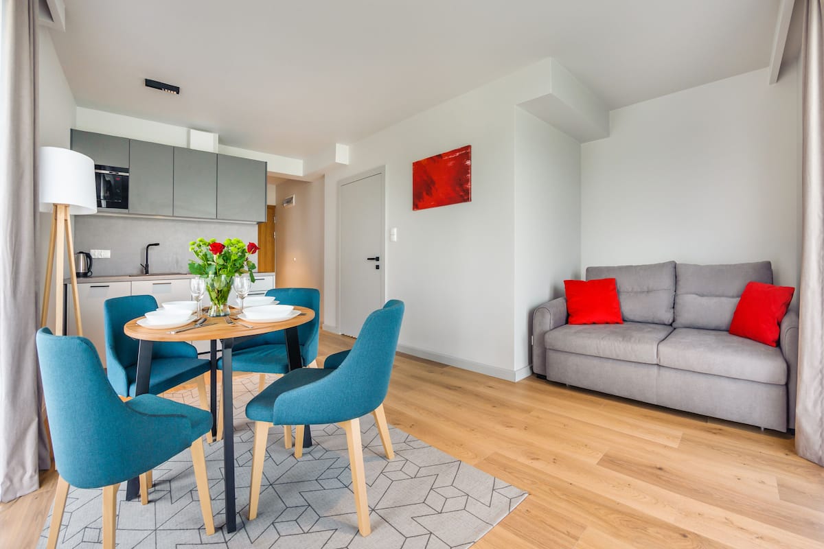 Uma sala de estar moderna com um sofá cinza, cadeiras verde-água e uma mesa de jantar posta para quatro pessoas.