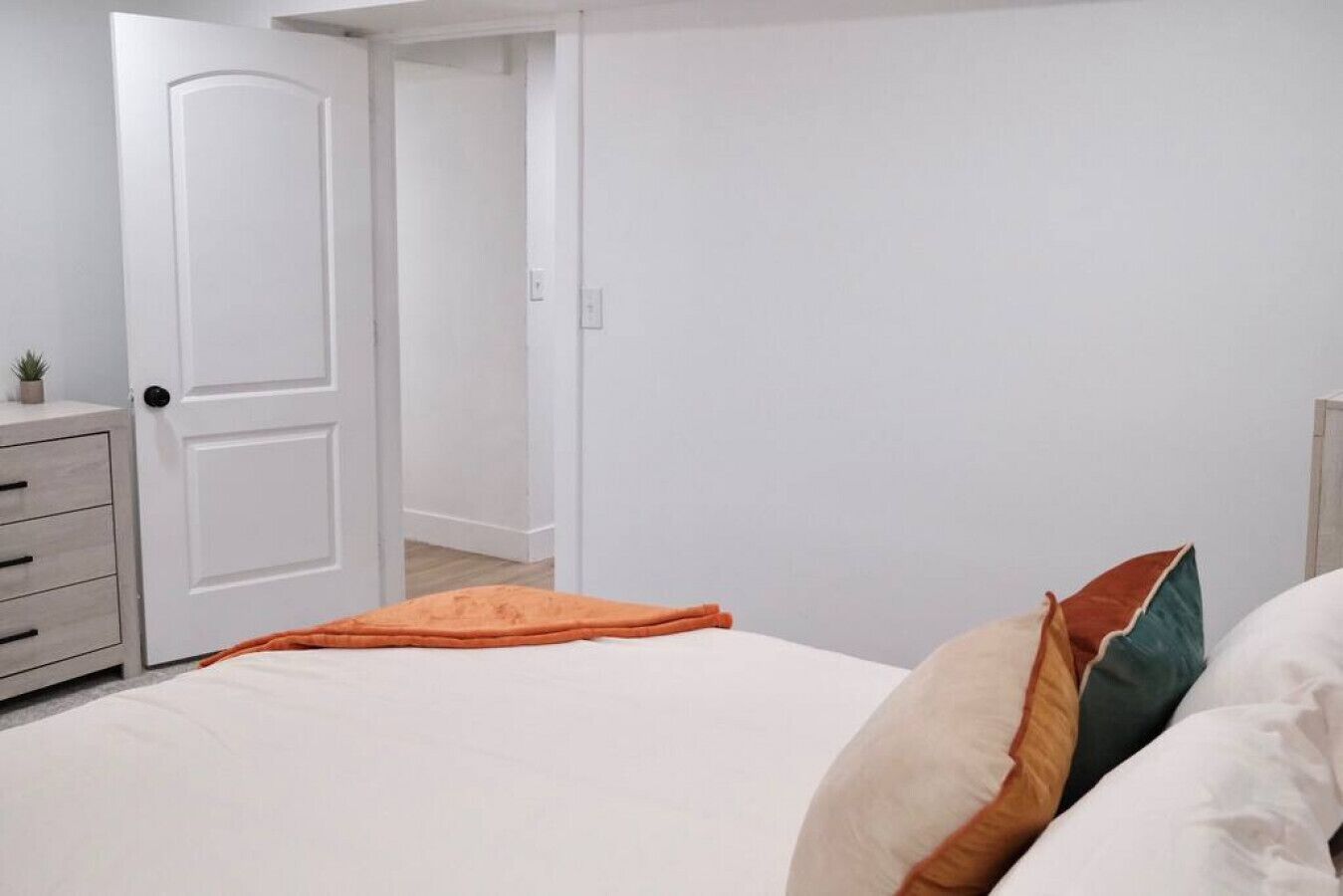 Un dormitorio con cama, mesita de noche, cómoda y puerta que da a otra habitación.