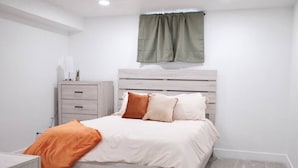 Ein Schlafzimmer mit einem Bett, einem Nachttisch, einer Kommode und einem Fenster mit Vorhängen.