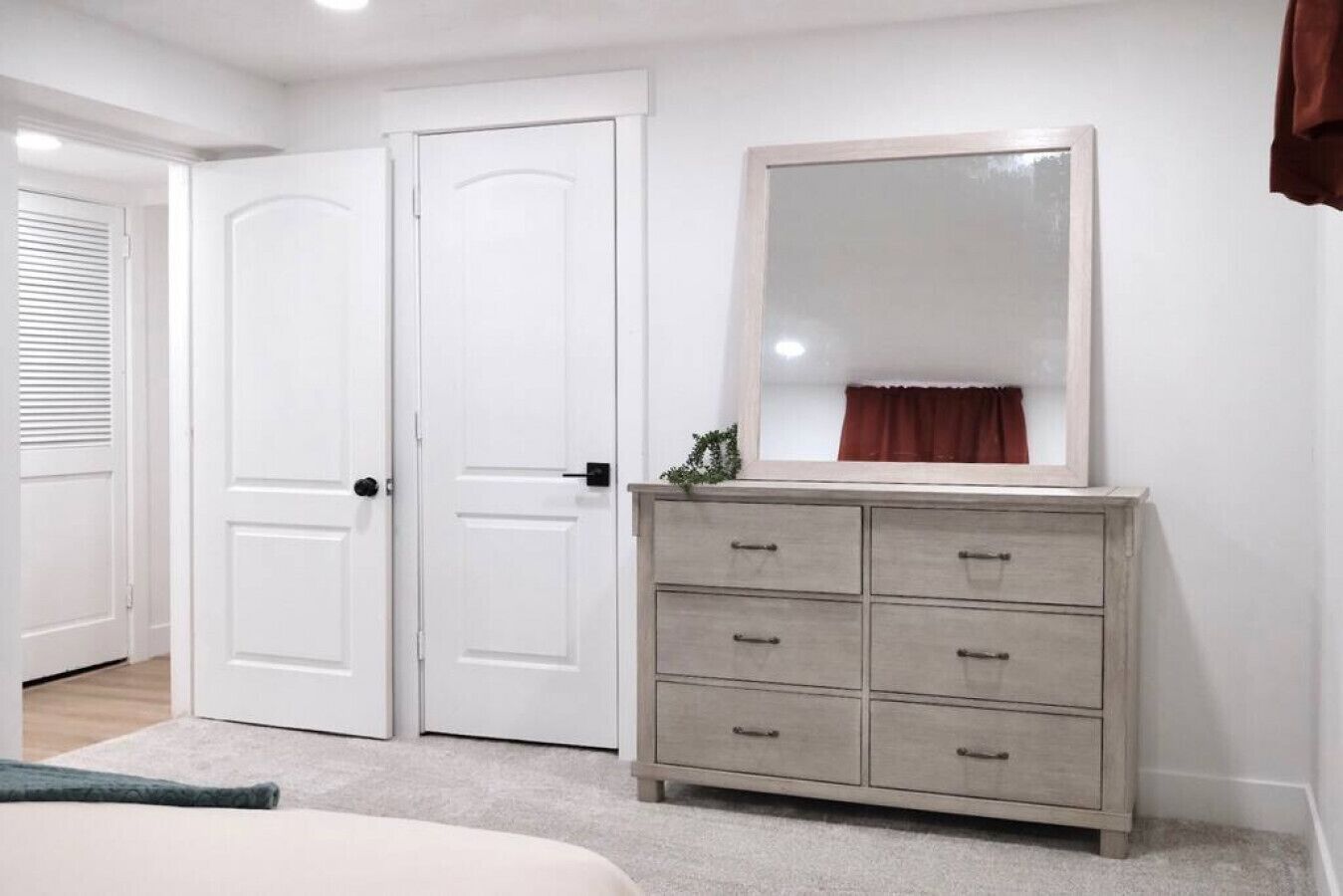 Un dormitorio con una cama, un aparador, dos puertas blancas y un espejo.