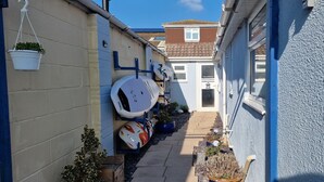 A narrow alleyway with a blue wall, a white door, and a small garden area with potted plants and a surfboard leaning against the wall. - Hayling Hideaway, private self contained cosy annex near to beach (Hayling Island)