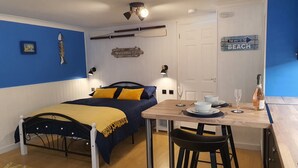 A bedroom with a bed, bedside table, and a small dining area with a table, chairs, and a bottle of champagne. - Hayling Hideaway, private self contained cosy annex near to beach (Hayling Island)