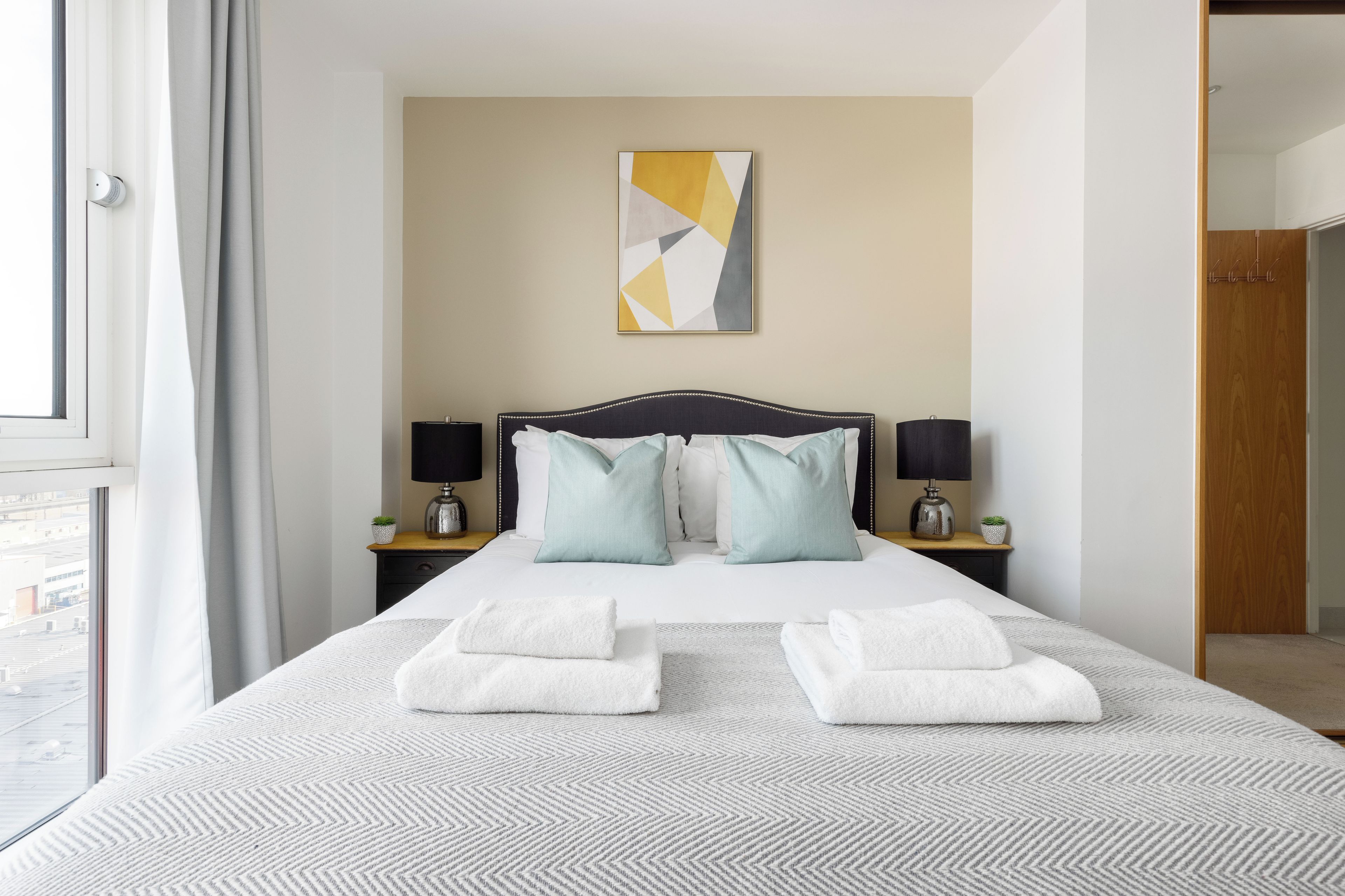 Una habitación de hotel con una cama, dos mesitas de noche, una lámpara, una obra de arte en la pared y vistas por la ventana.