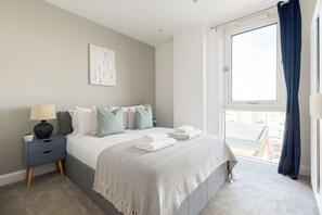 Une chambre à coucher avec un lit, une table de chevet, une lampe et une fenêtre avec des rideaux.