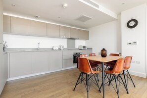 Uma cozinha moderna com armários cinza, uma mesa de jantar de madeira com quatro cadeiras e um relógio fixado na parede.