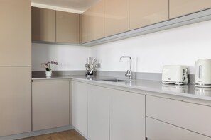 Cozinha moderna com armários brancos, uma pia de aço inoxidável e dois eletrodomésticos brancos na bancada.