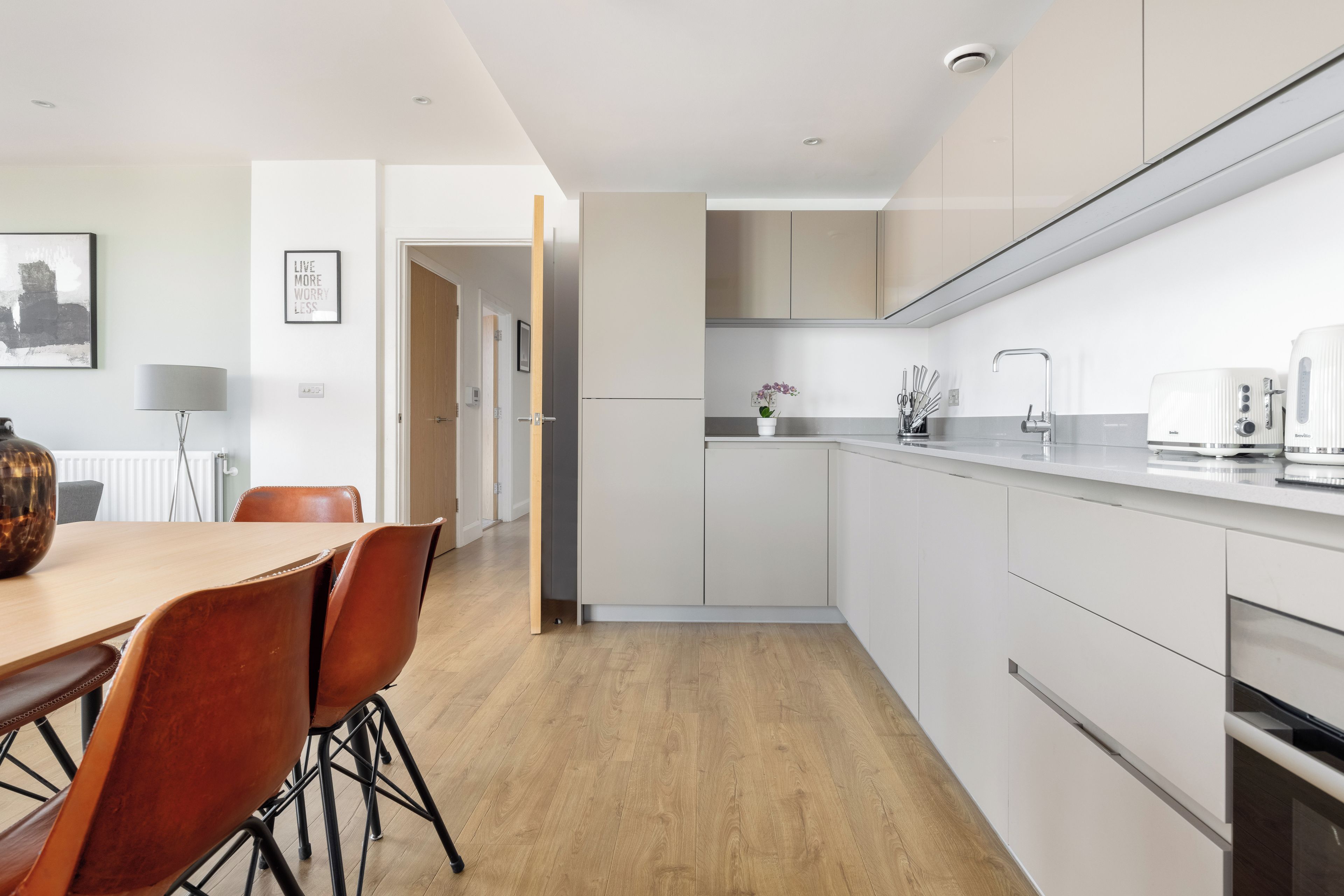 A modern kitchen with white cabinets, a wooden dining table with chairs, and a coffee maker.