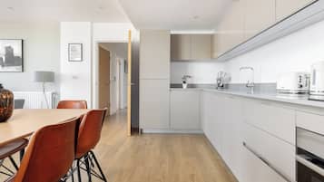 A modern kitchen with white cabinets, a wooden dining table with chairs, and a coffee maker.