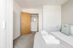 Quarto moderno com porta de madeira, cama com toalhas dobradas, radiador e um mapa emoldurado na parede.