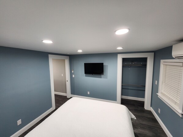 Un dormitorio con cama, armario, televisor e iluminación empotrada en el techo.