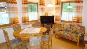 A cozy living room with a round wooden table, chairs, a sofa, and a television. - Appartement im 1.0g- - Urlaub auf dem Aignerhof (Muhr)