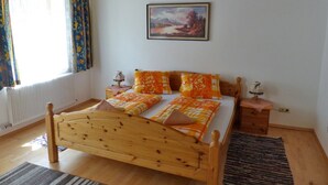 A wooden bed with a headboard, two bedside tables, a window with curtains, a radiator, and a painting on the wall. - Appartement im 1.0g- - Urlaub auf dem Aignerhof (Muhr)