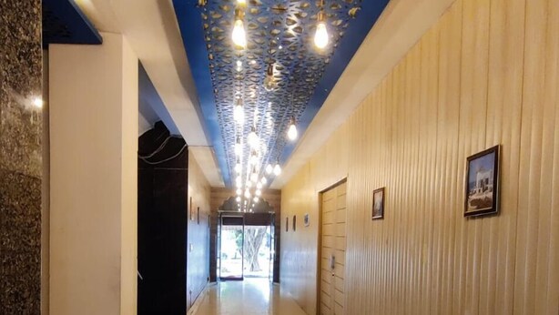 A hallway with a blue ceiling, wooden paneling, and a tiled floor. - Hotel Rivasa Regency (New Delhi)