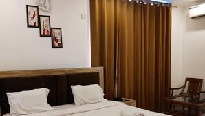 A neatly made bed with white linens, a wooden headboard, and a bedside table with a lamp. - Hotel Rivasa Regency (New Delhi)