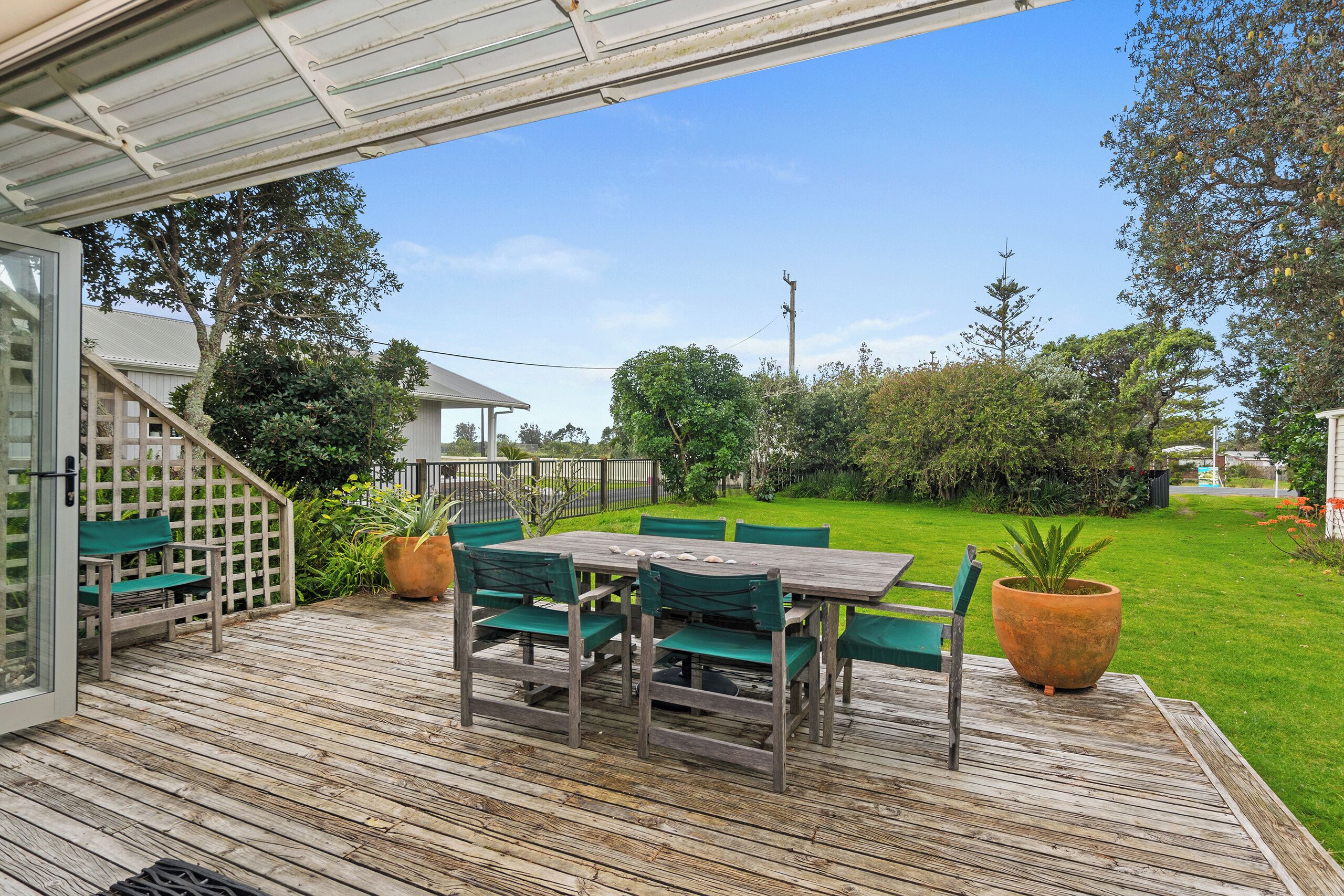 A wooden deck with a table and chairs, surrounded by greenery and a clear sky.