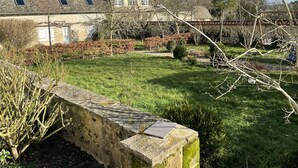 A stone building with a sloped roof, a garden with grass and shrubs, and a stone wall in the foreground.