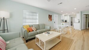 Ein modernes Wohnzimmer mit grauem Sofa, einem Couchtisch und einem Essbereich mit weißem Tisch und Stühlen.