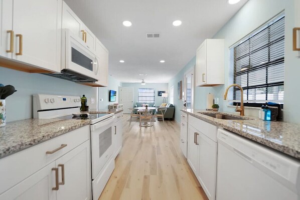 A modern kitchen with white cabinets, granite countertops, and a central island. - Coconut Grove - Your holiday beach getaway! (St. Augustine Beach)