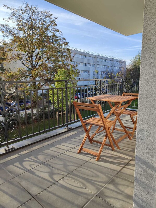 Un balcon avec un sol carrelé, une table en bois et deux chaises.