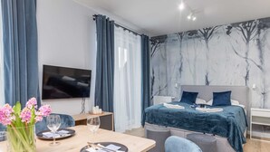 A modern bedroom with a bed, a TV, a dining area with a table and chairs, and a wall with a tree mural.