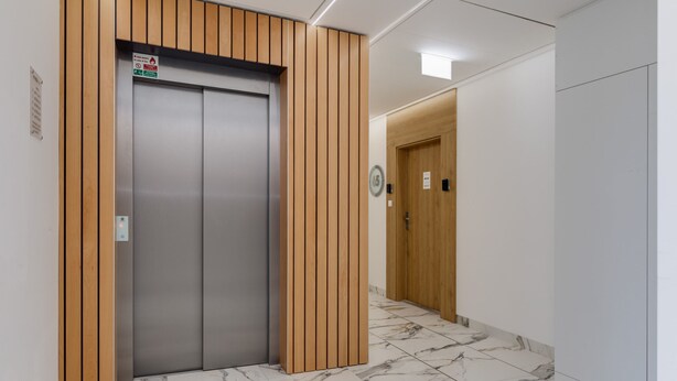 Un moderno ascensor con paneles de madera, suelo de baldosas de mármol y una pared lisa con una puerta al fondo.