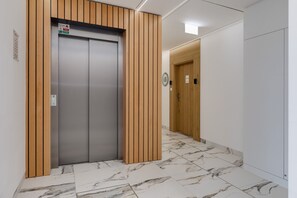 Un ascenseur moderne doté de panneaux en bois, d’un sol carrelé en marbre et d’un mur sobre avec une porte en arrière-plan.