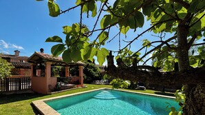 Una piscina cristalina rodeada de un césped bien cuidado, una zona de terraza cubierta y un muro de piedra.