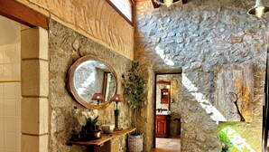 Un pasillo de paredes de piedra con un banco de madera, un espejo y una planta en maceta.