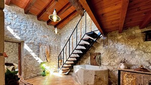 Un interior rústico con pared de piedra, escalera de madera y suelo de baldosas.