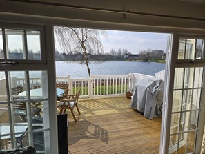 A deck with a table and chairs, a grill, and a view of a lake. - Luxurious South-Facing Lakeside Lodge (Cirencester)