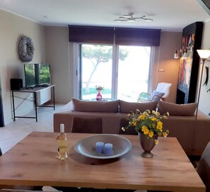 Ein modernes Wohnzimmer mit einer Couch, einem Esstisch mit Blumenvase und einem Fernseher auf einem Schrank.