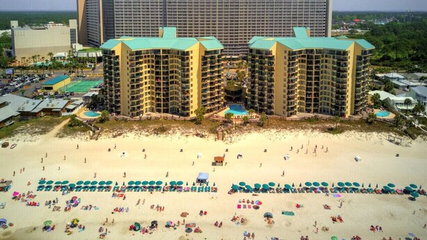 A beachfront hotel with multiple high-rise buildings, a sandy beach, and numerous umbrellas.