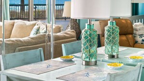 A dining area with a table set for two, a view of the ocean through large windows, and a cozy seating area with a sofa and chairs.