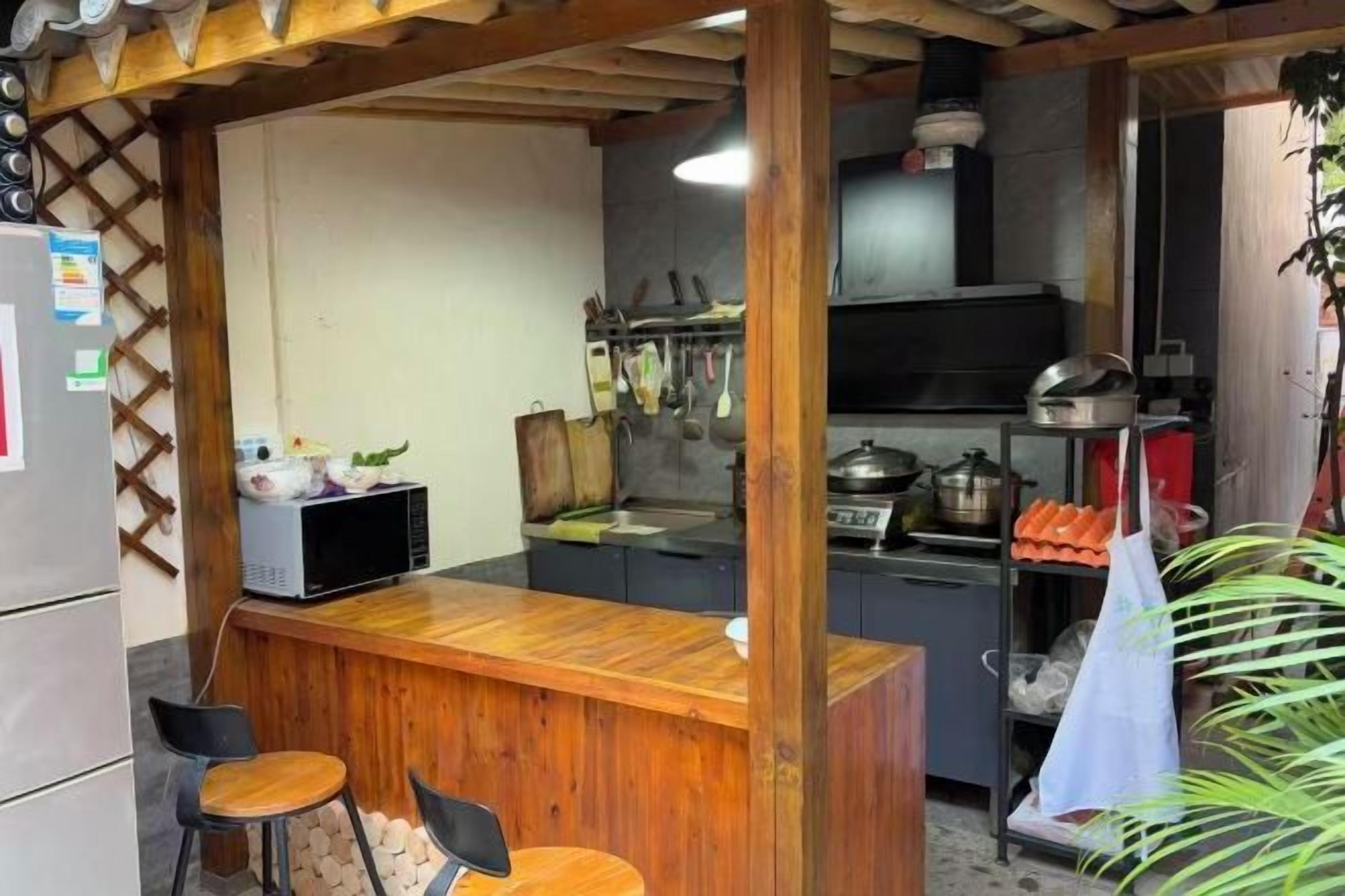 A kitchen with a wooden bar counter, two stools, a refrigerator, and a sink.