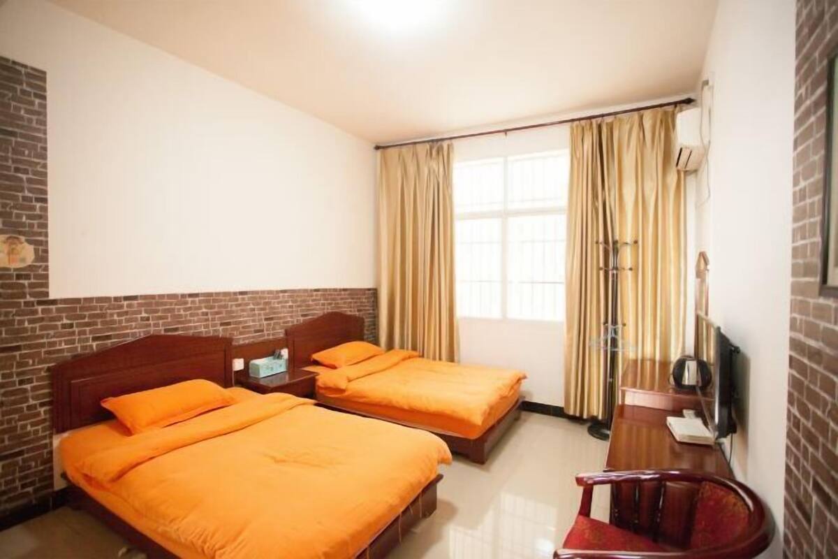 A hotel room with two beds, a desk, a chair, a TV, and a window with curtains.