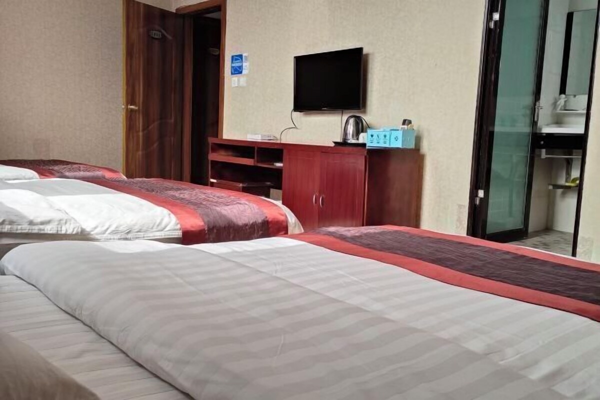 A hotel room with two beds, a TV, a minibar, and a bathroom visible through a glass door.