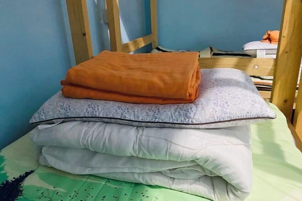 A bed with a folded orange blanket, a grey patterned pillow, and a white pillow on a green bedspread.