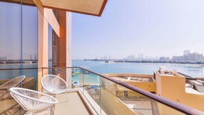 A balcony with two white wire-framed chairs, a glass railing, and a view of a city skyline and water body. - Tiara - Luxury Palm Jumeirah (Dubai)