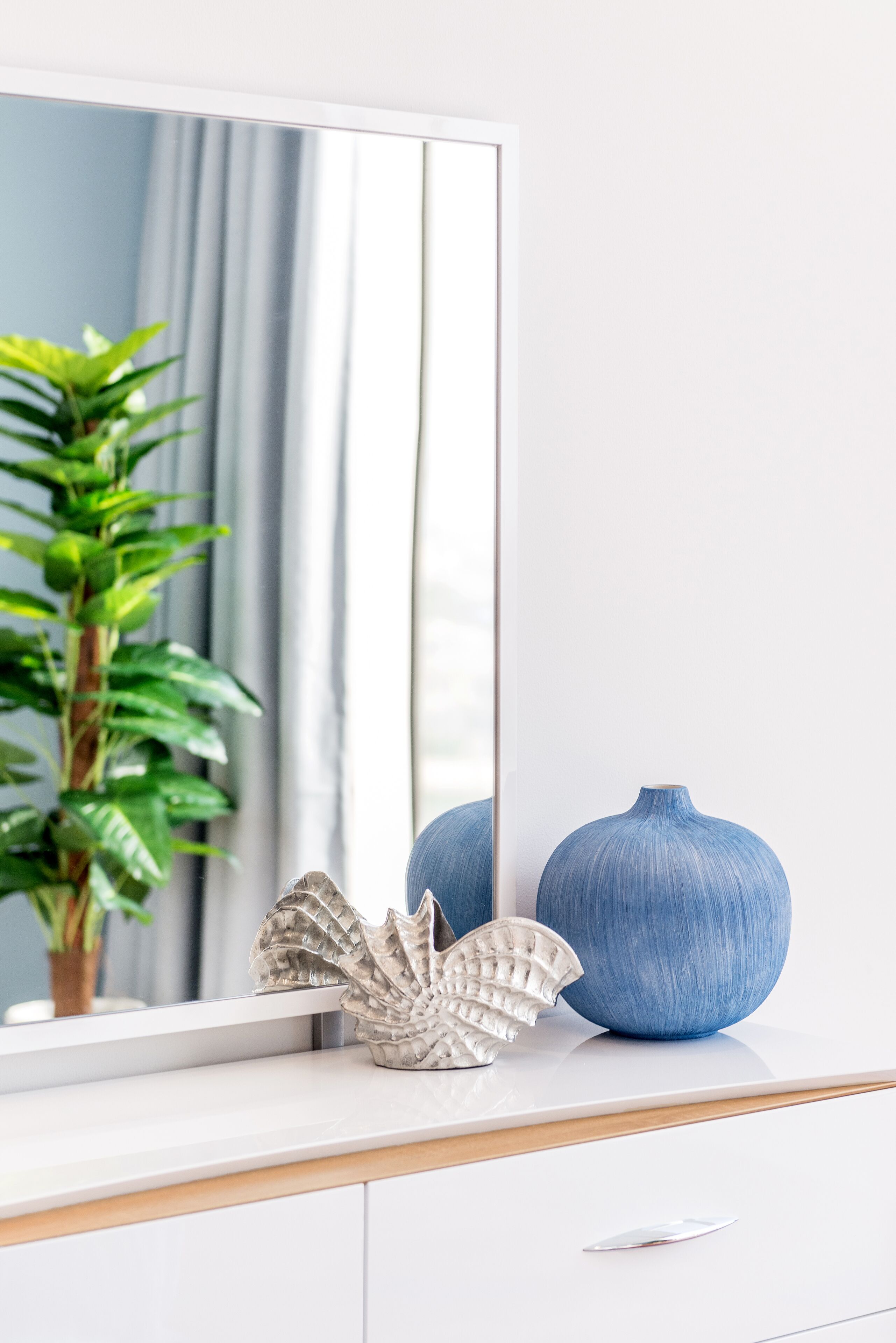 A white vanity with a mirror, a blue vase, and a decorative shell.
