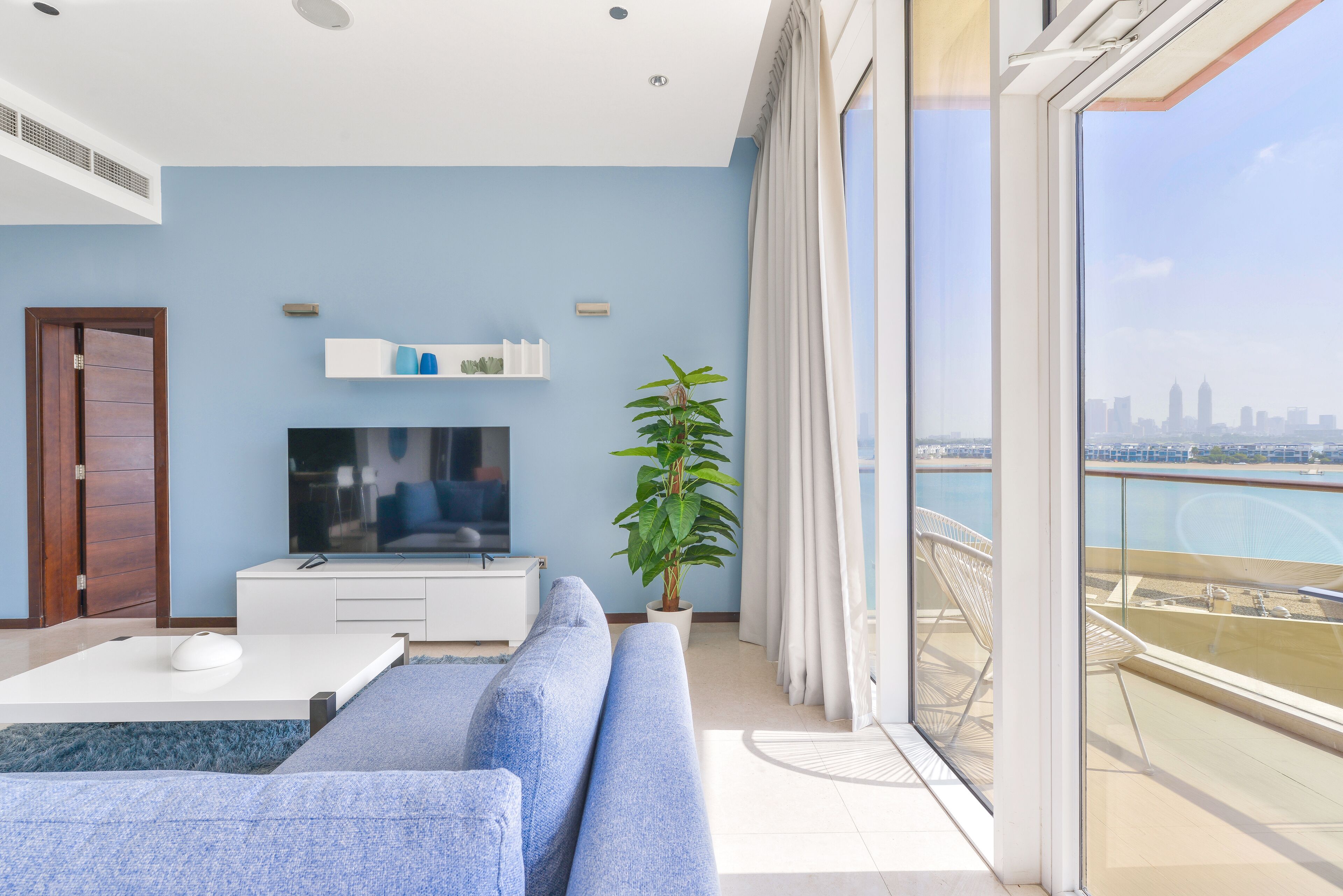 A modern living room with a flat-screen TV, a sofa, a coffee table, and a potted plant.