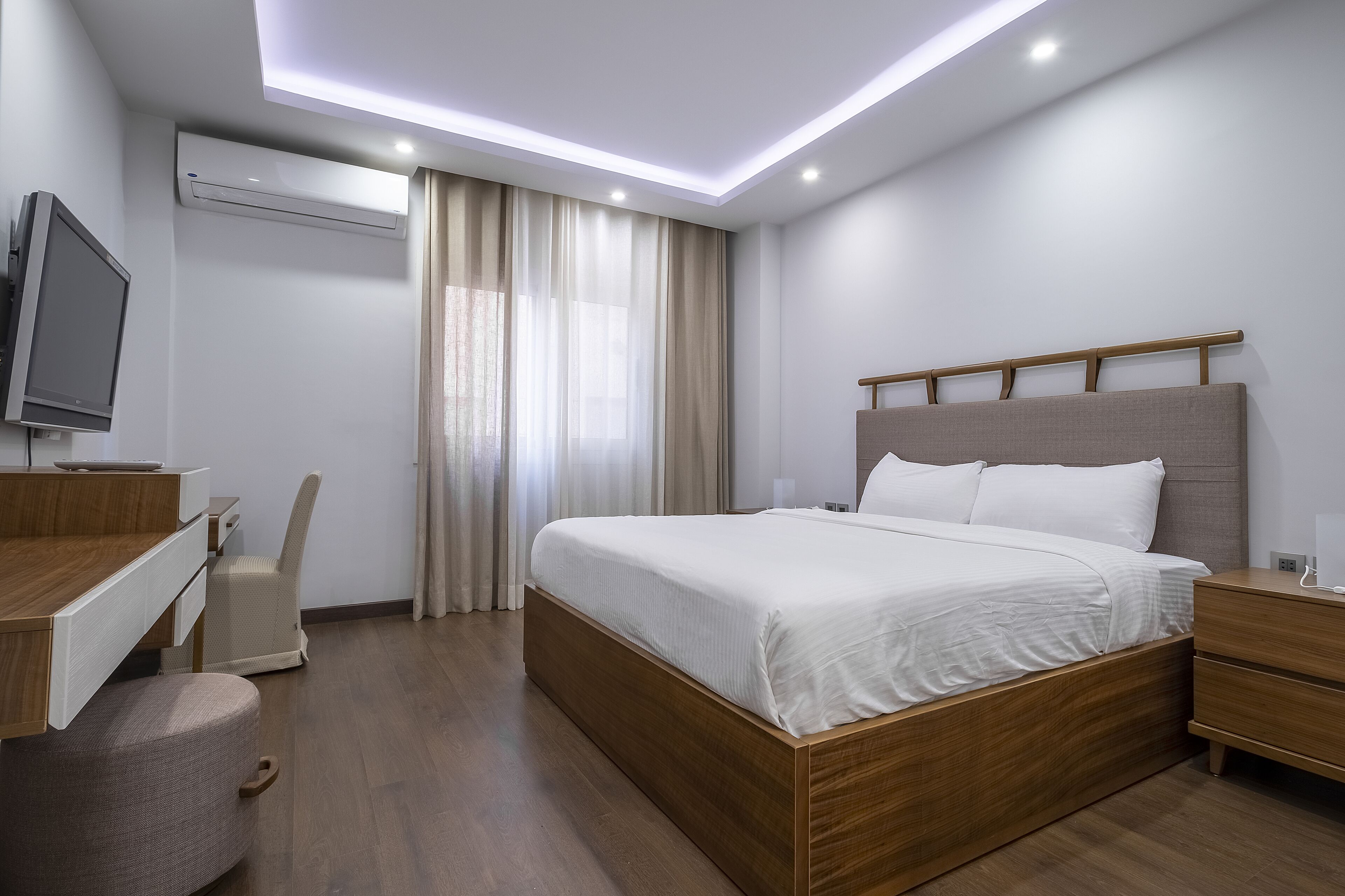 Une chambre d’hôtel moderne avec un lit en bois, un bureau avec une chaise, une télévision et un appareil de climatisation.