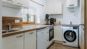 A compact kitchen with white cabinets, a built-in dishwasher, a washing machine, and a coffee maker. - Dahuam am Weinberg - Inner warmth (Winten)
