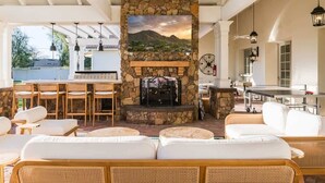 A covered outdoor seating area with wicker furniture, a stone fireplace, and a view of the landscape. - Chateau D`Arcadia - A French Inspired Luxury Home (Scottsdale)